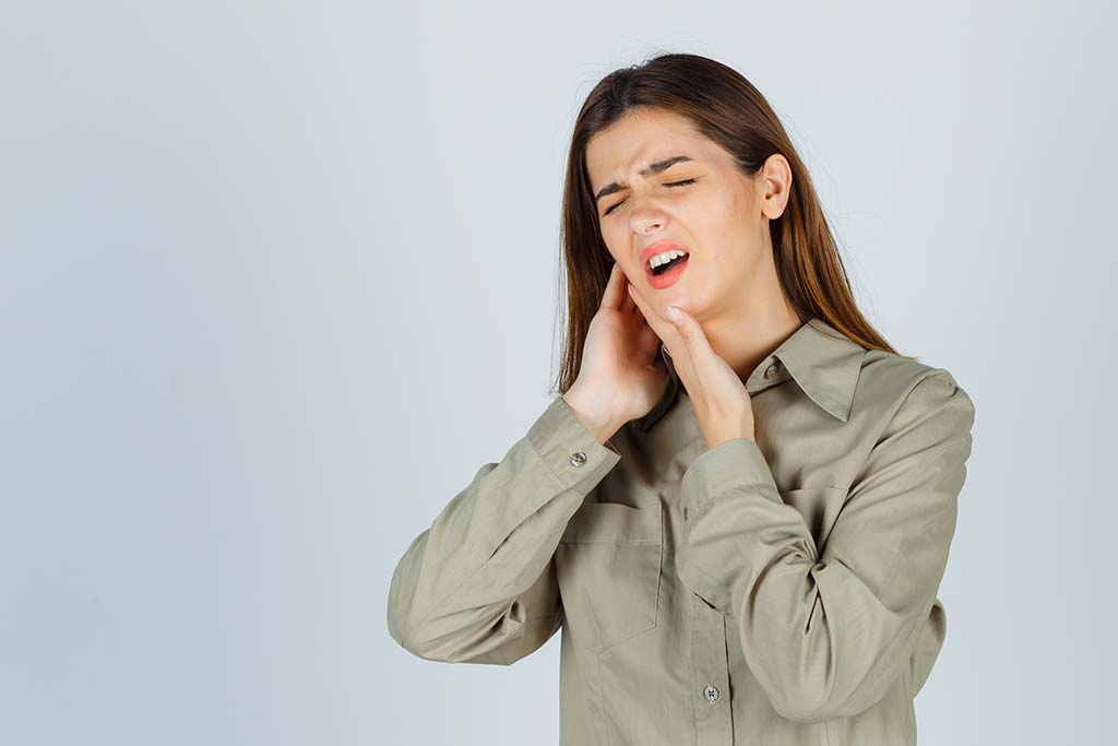 Mujer con diabetes tocándose la mandíbula por dolor dental, representando problemas de encías en Albacete.